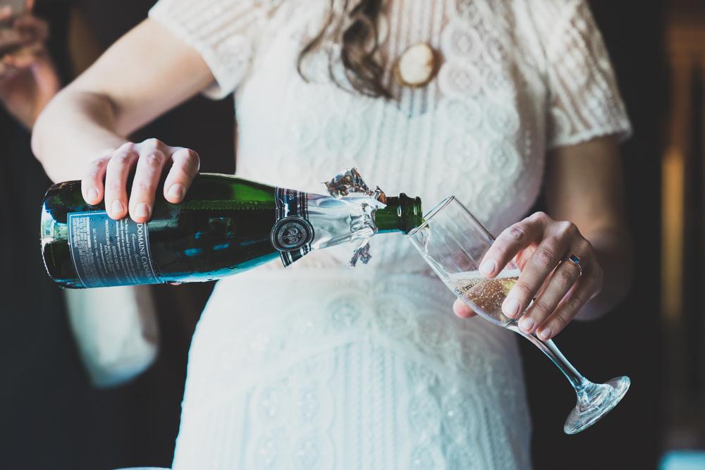 Bride pouring champagne during cabin inspired summer wedding