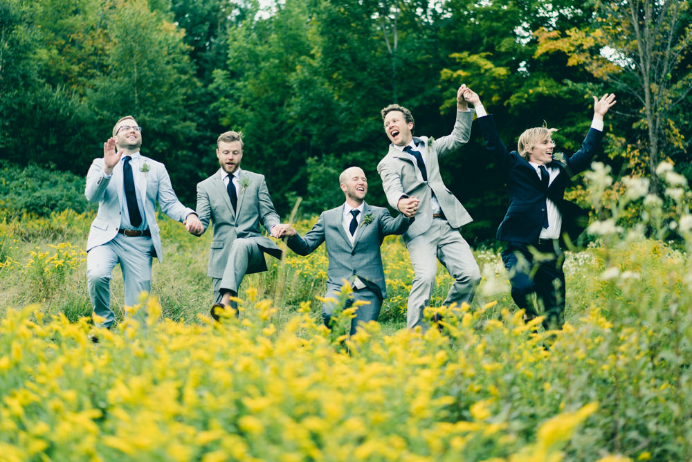 Funny and creative shot of groomsmen holding hands and jumping through field of flowers