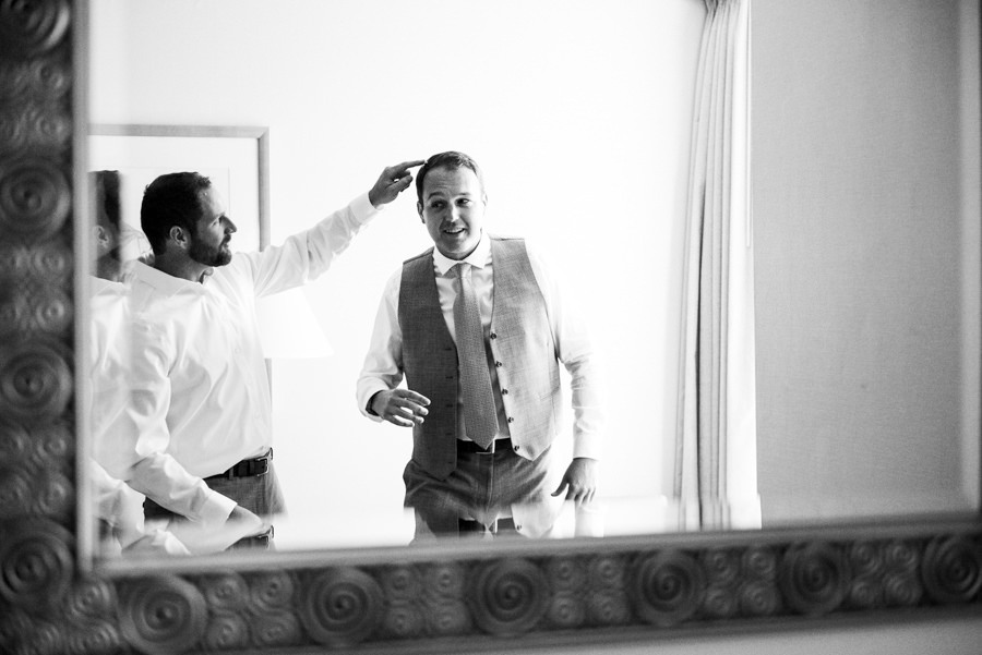 black and white candid portrait of groomsmen helping groom with hair