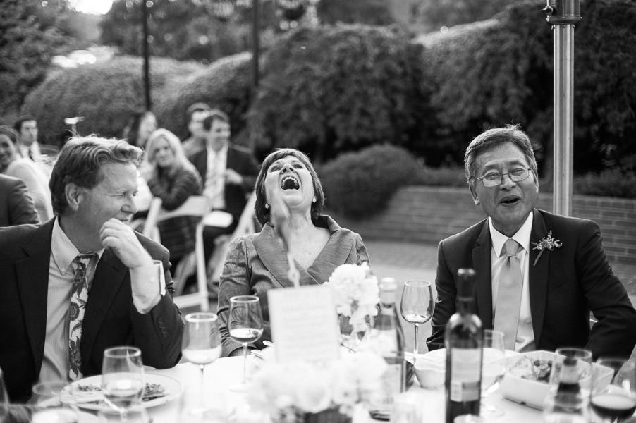 Black and white candid portrait of bride's parents laughing during wedding dinner at Piedmont Community Center