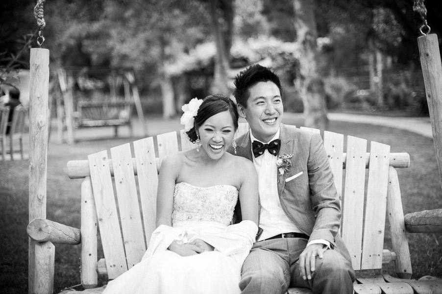 black and white candid portrait of bride and groom laughing on bench at Saddlerock Ranch wedding in Malibu