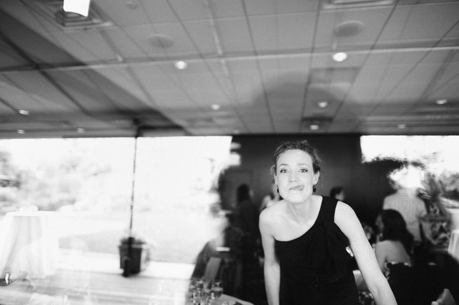 Black and white candid portrait of guest sticking out her tongue through window during wedding